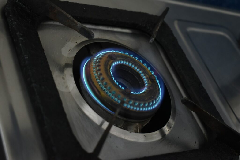 Burner kompor gas menyala dengan api biru pada komponen kompor gas